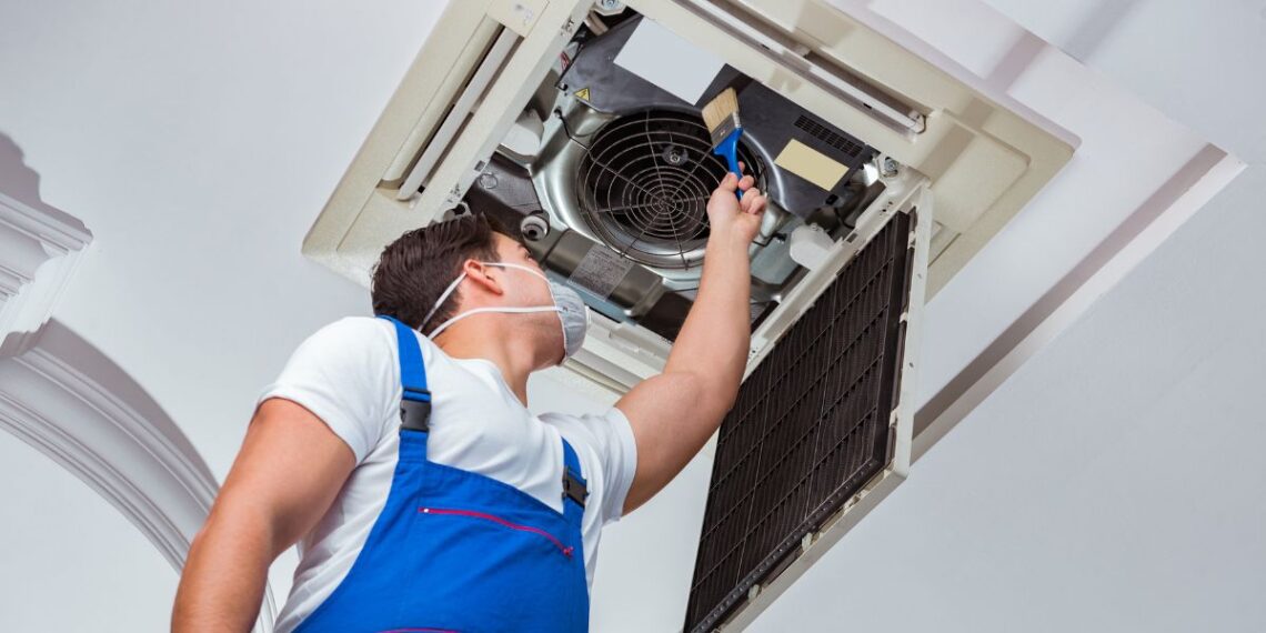 A technician in overalls and an apron is repairing an air conditioner.