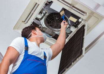 A technician in overalls and an apron is repairing an air conditioner.