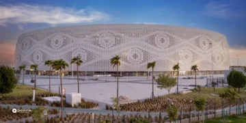 Al Thumama Stadium in Doha, Qatar, captured at sunset. The stadium features an iconic circular design inspired by traditional Gahfiya headwear, surrounded by palm trees and landscaped walkways. A key venue for Qatar’s sporting legacy and future Olympic ambitions.